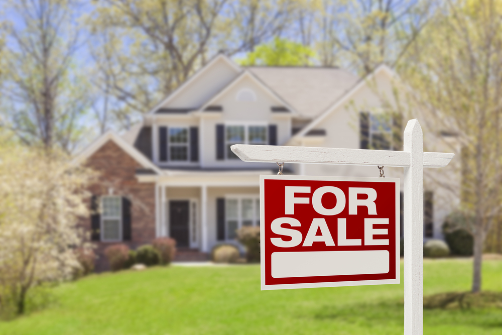 For sale sign in front of home, bright spring day.