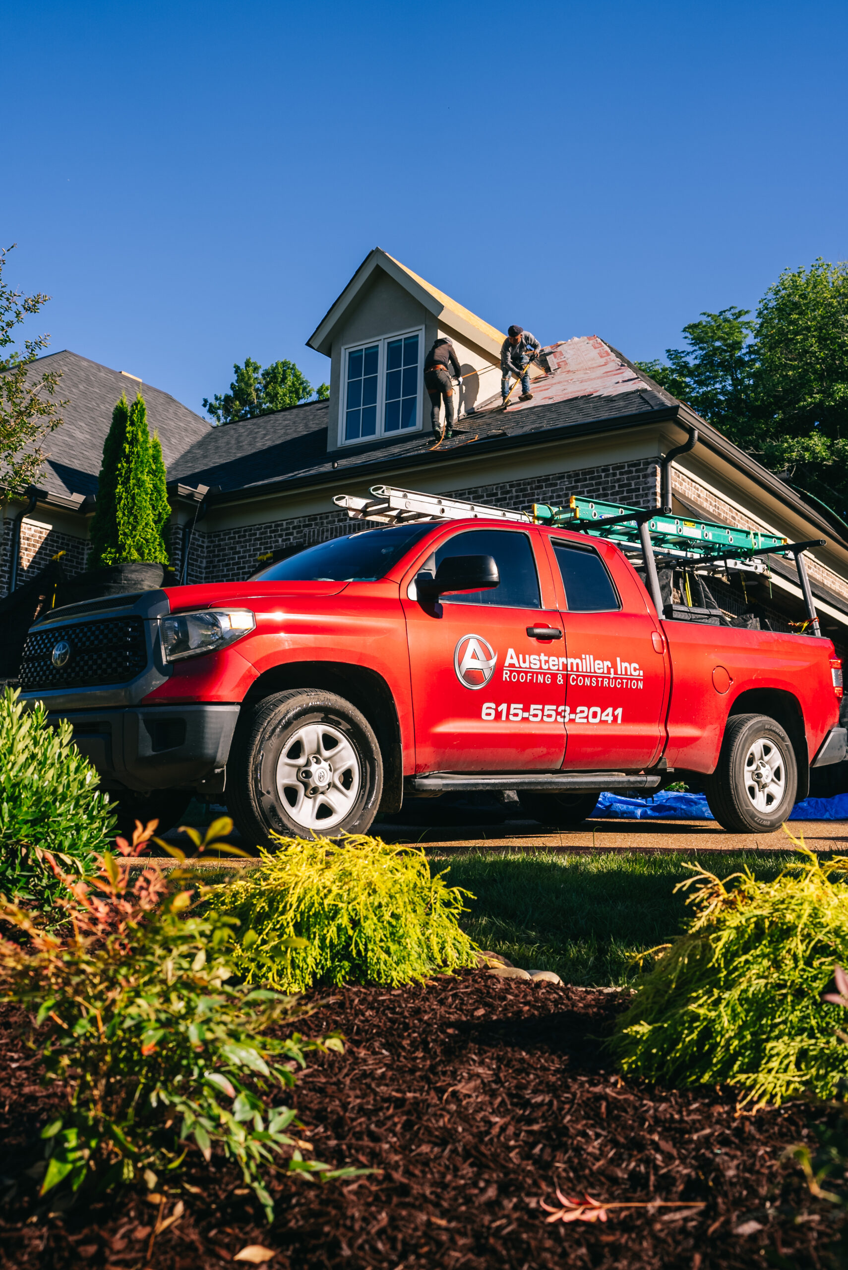 Red Austermiller truck in front of home under roofing construction.