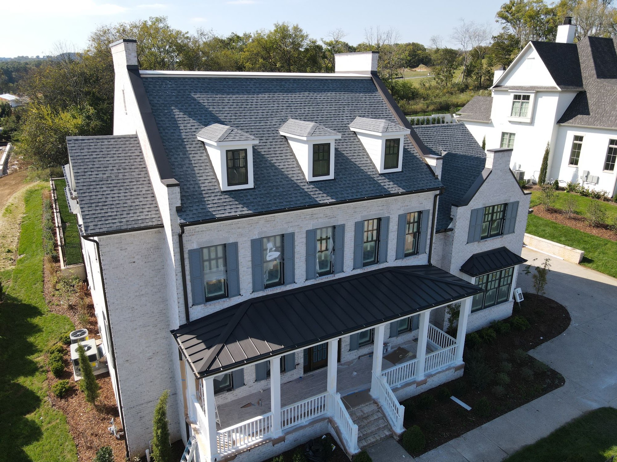 Aerial view of a two-story white brick Tennessee home with a dark gray architectural asphalt shingle roof and dormers