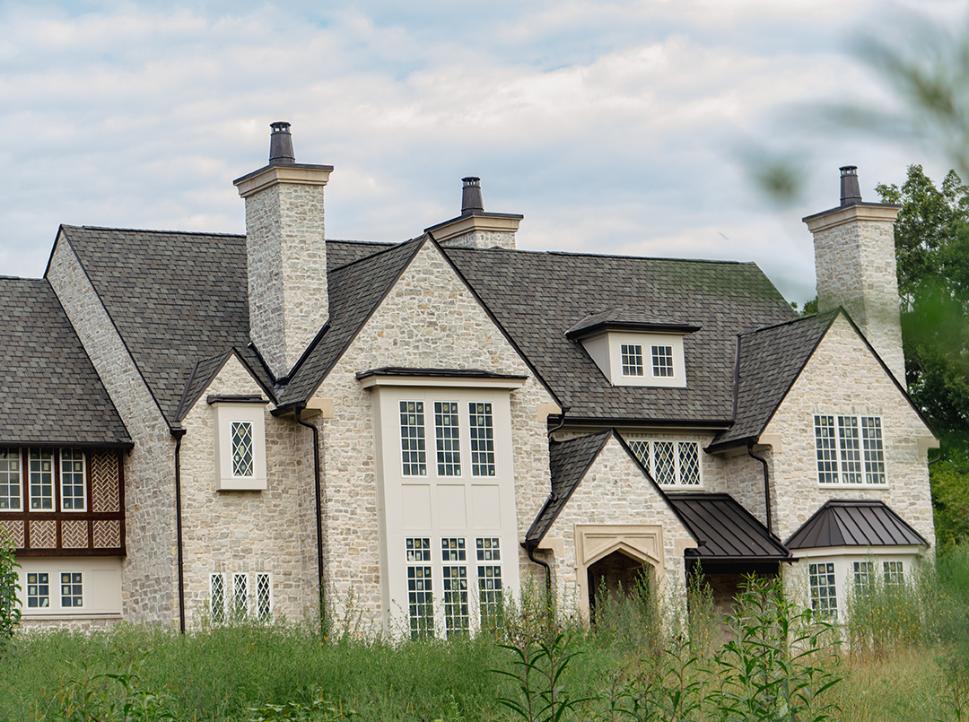 Stone Tennessee home with a dark asphalt shingle roof, multiple chimneys and standing seam metal accents